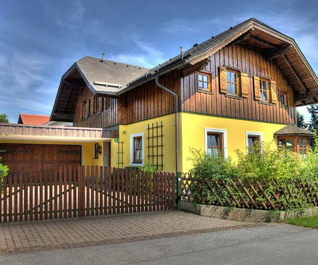  Vorderansicht eines gelben Hauses, umgeben von einem rustikalen Holzzaun.