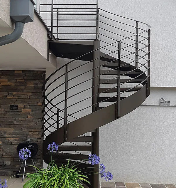 Eine spiralförmige Treppe vor einem Haus, die elegant in den Eingangsbereich führt.