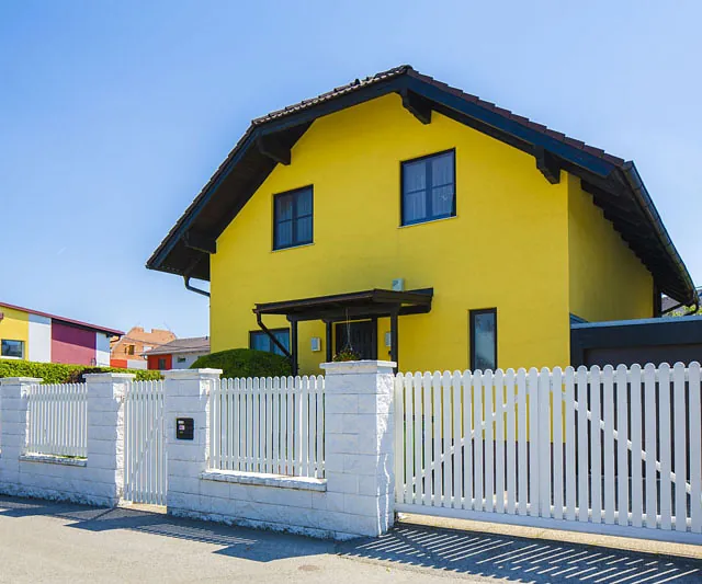 Ein gelbes Haus mit einem weißen Zaun umgibt die Vorderansicht des Gebäudes.
