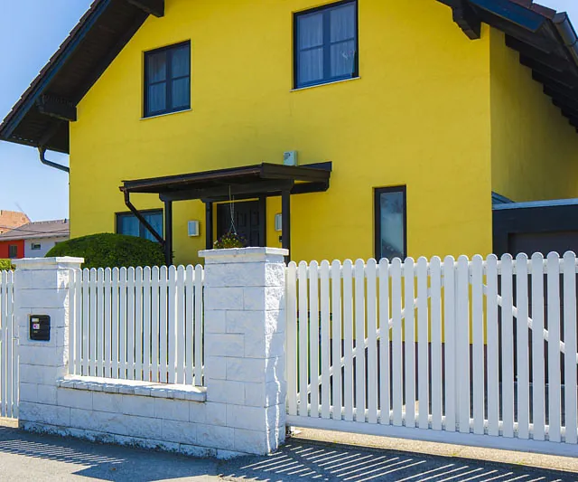  Ein gelbes Haus mit einem weißen Zaun umgibt die Vorderansicht des Gebäudes.