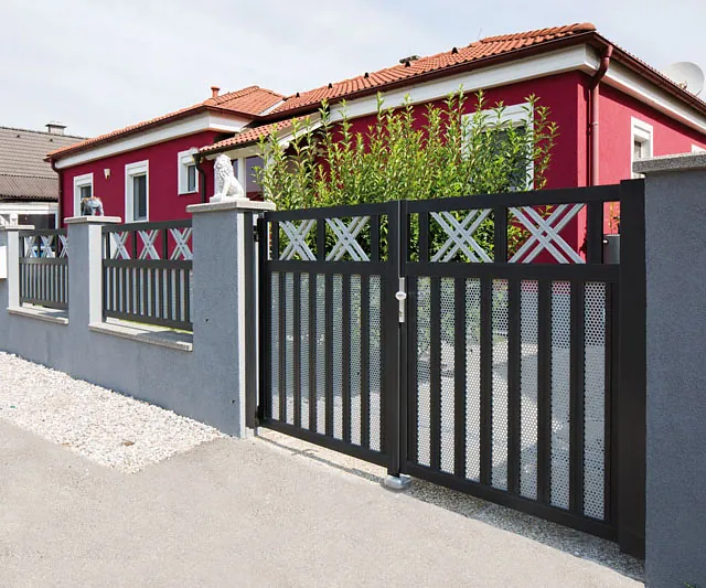 Ein Zaun mit einem roten Haus im Hintergrund.