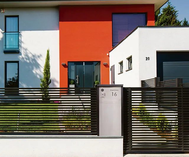 Ein schwarzer Zaun und eine rote Tür an einem weißen Haus.