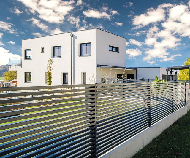 Ein modernes Wohnhaus, während eine Katze am Zaun vorbeiläuft.