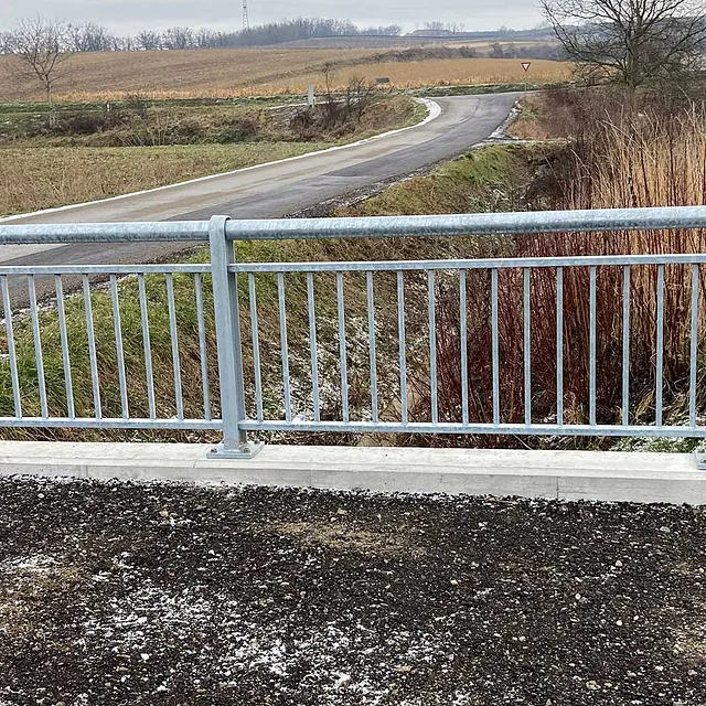 Metallzaun an einer Straße, neben einem weitläufigen Feld.