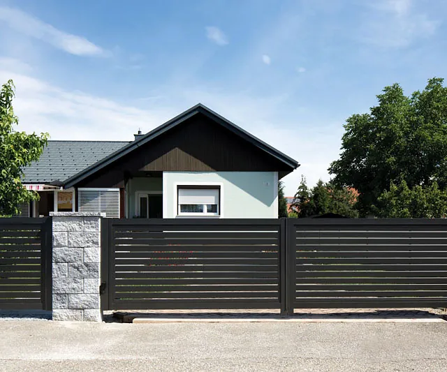 Ein Haus mit einem schwarzen Tor und einem Zaun umgibt das Grundstück.