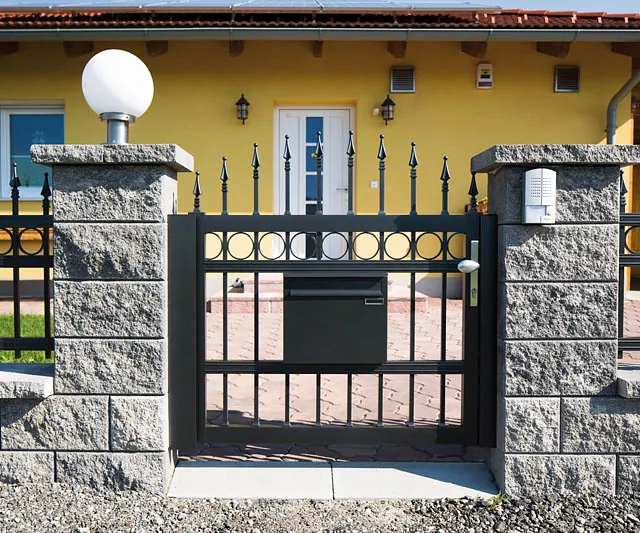 Ein schwarzer, kunstvoller Schmiedeeisenzaun, der einen Bereich abgrenzt und eine dekorative Funktion hat.